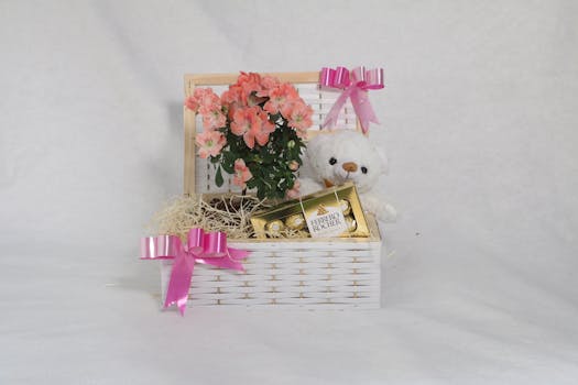 Panier gourmand sans gluten avec fleurs roses, un ours en peluche et des douceurs, décoré de rubans roses.